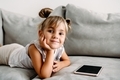 Toddler girl  lies on couch at home and playing with digital wireless tablet computer. - PhotoDune Item for Sale