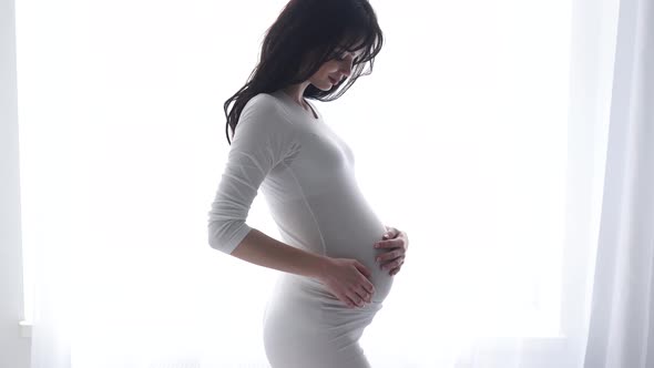 Pregnant Woman Touching Baby Belly In White Interior