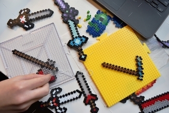 word, pickaxe and axe weapons and patterns using perler beads. Fusible colorful bead. Toy that develops the imagination and creativity of child. Children`s or boy’s toys and craft theme or concept
pixel art swords crafting craft crafts design at home activity Caucasian close ironing creative top view overhead from above hobby kid hama art diy do it yourself artisinal crafting childhood concentration fun inspiration hands