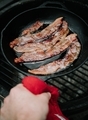 Cooking bacon in a cast iron skillet at a campsite.  - PhotoDune Item for Sale