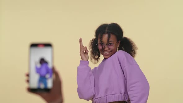 Cheerful African Girl Dances to the Music on a Beige Background While Shooting a Video on Smartphone