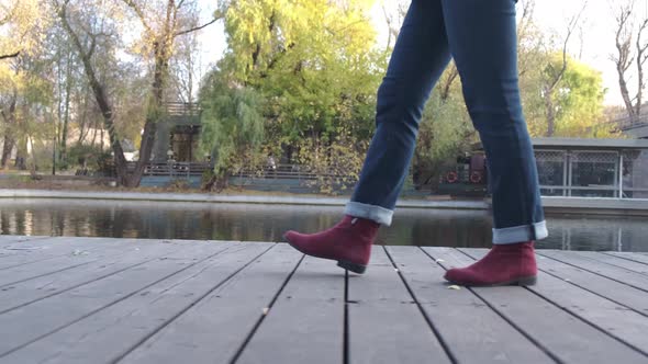 Female Legs in Burgundy Boots and Blue Jeans Climb the Stone Stairs