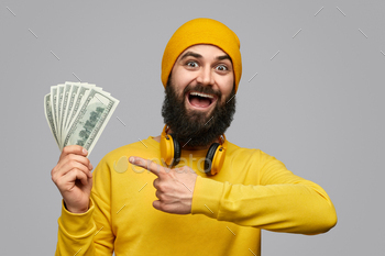 at camera and pointing at money while demonstrating earnings against gray background