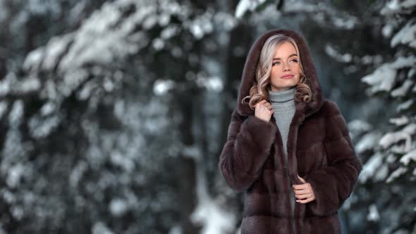 Pleasant Blonde Female Posing in Luxury Hood Fur Coat Natural Forest