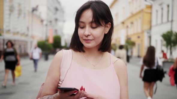 Smiling Mixed Race Woman Tourist Using Mobile Phone Typing Text Messages Walking in the City Center