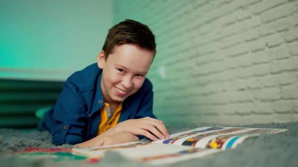 Happy boy lying on bed reading book at home. Home education.