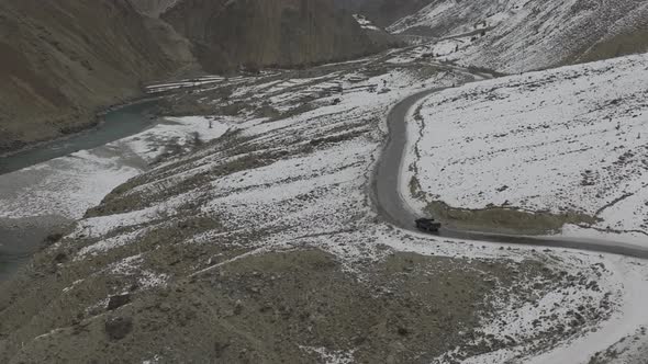 Aerial Drone View Of Black SUV Driving Winding Snow Rocky Mountain Roads In Winter Through Hunza Val