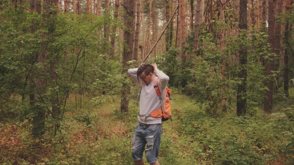 Young Traveling Man with Backpack Scaring Insects Away From Himself in Green Summer Forest