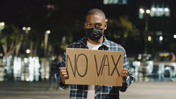 Young Angry African American Man in Black Mask Stands in City at Night Evening Holding Sign Banner