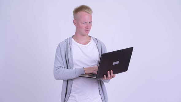 Happy Young Blonde Handsome Man Thinking While Using Laptop