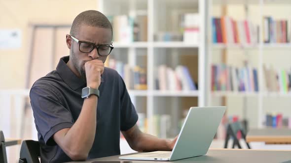 Exhausted African Man Working on Laptop and Coughing in Library