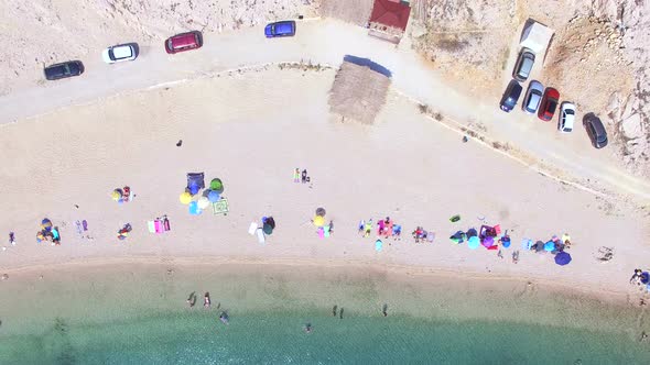 Flying above parked cars and people on sandy beach of Pag island