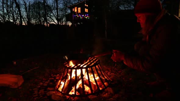 Illuminated treehouse at night, woman at bonfire