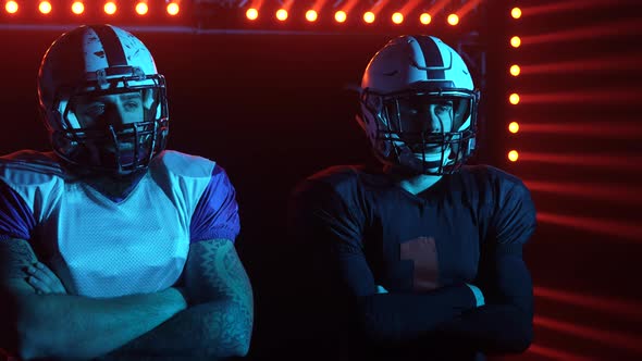 Two Confident Professional Quarterbacks Stand on the Field Against a Backdrop of Red Light and Smoke