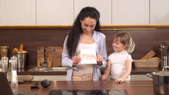 Mom Gets a Greeting Card From Her Daughter with a Heart While Cooking Together in the Kitchen