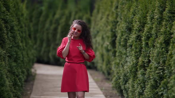 Young Woman is Walking in Park and Talking By Phone Resting in Summer Day