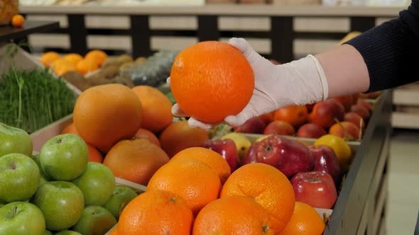 Closeup of a Woman in Rubber Gloves Holding an Orange in a Grocery Store