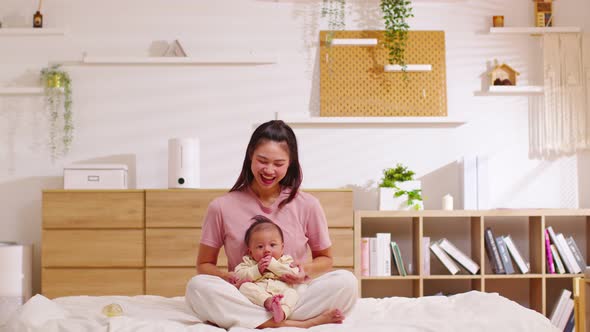 Beautiful Asian mom woman holding newborn baby in her arms sit on bed at white cozy home.