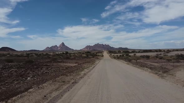 Drone footage of a long road in the desert with huge Erongo mountains