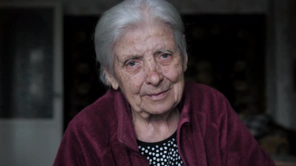 Portrait Of Old Woman With Tremor Nervous Tic Looking At Camera Sitting At Home