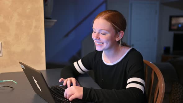 a young girl looks up from her computer, smiles, and shakes her head agreeing with the viewer