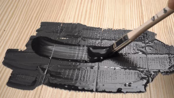 Paint brush draws in black bold strokes on a wooden board canvas