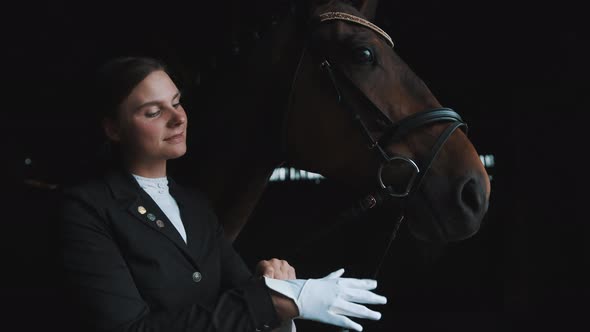 Horsewoman Standing With Her Dark Brown Horse In The Stable Putting On Her Gloves