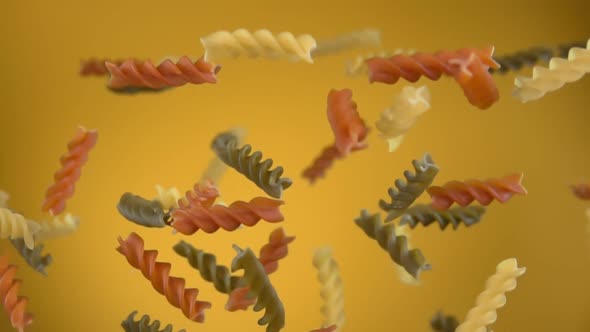 Dry Colored Pasta Fusili Flying Up on a Yellow Background