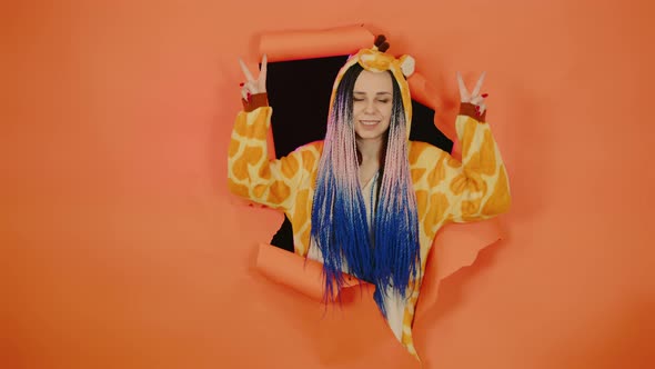 Young Woman in Pajamas of Giraffe Posing in Hole of Orange Background