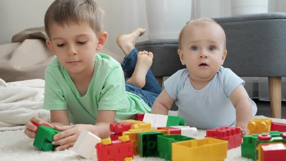 Little Baby Boy with Older Brother Playing Toy Blocks and Bricks on Carpet in Living Room