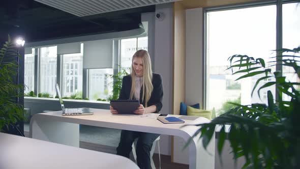 Stylish Business Woman with Tablet in Office. Elegant Woman in Suit Sitting at Table with Laptop and