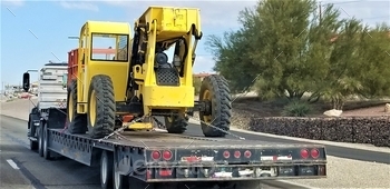  towing a low boy trailer with a big yellow bucket lift, to deliver to a construction site.