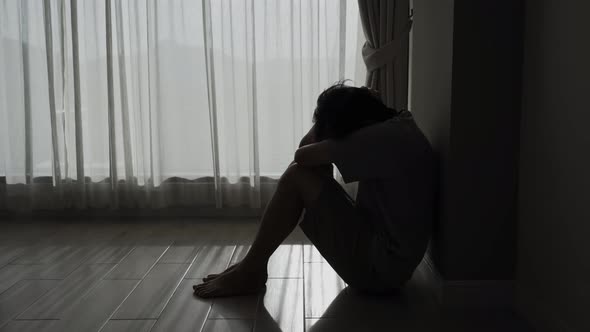 Lonely young man feeling depressed and stressed sitting in the dark bedroom