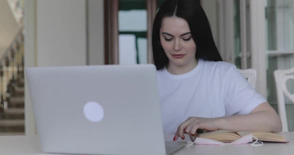 Attractive Girl Communicates on the Internet at Table with Equipment in Room