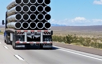  hauling a flat bed trailer filled with construction pipes.