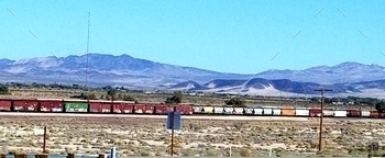 es of cars, on the railroad tracks in a rural landscape with a mountainous backdrop.
