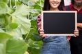 Close-up of beautiful smiling woman holding an empty blank black board inside green natural farm - - PhotoDune Item for Sale