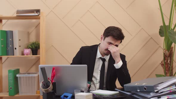 Office worker man hold glasses in one hand, is sitting at table with laptop