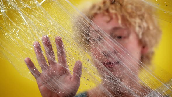 Closeup Male Caucasian Hand Touching Wet Food Film with Blurred Man at Yellow Background