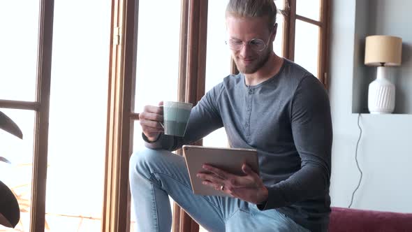 Man holds a digital tablet and drinks a hot drink