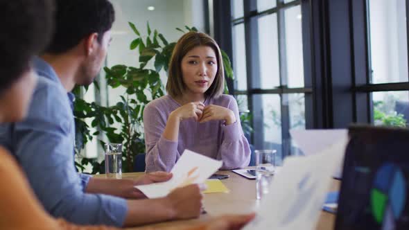 Diverse business people sitting using laptops going through paperwork in office