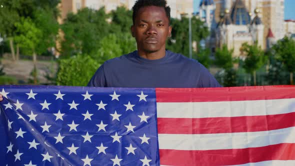 Camera Zoom in Patriot AfroAmerican Man Holding American Flag and Looks Camera