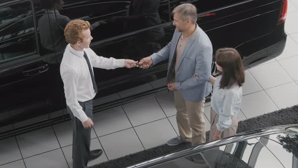 Salesman Handing Keys from New Car to Customers