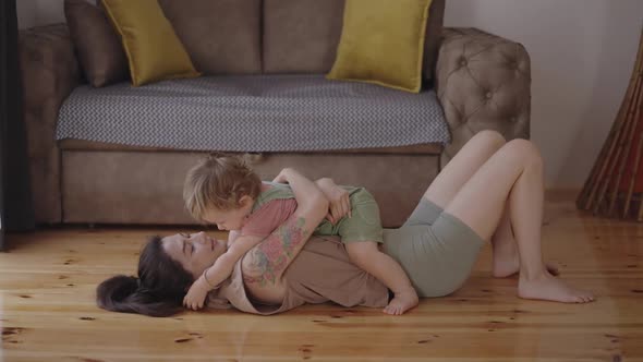 Happy Carefree Mother and Cute Small Child Daughter Tickling Laughing Having Fun Lying on Sofa and