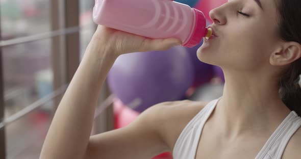 Tired Woman Drinks Water After Fitness Workout in the Gym