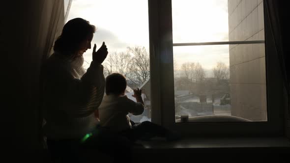 Mom and Son Sitting on the Big Window of the House in the Winter