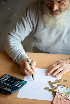 le concept – close up of old senior man hands with calculator and bills counting euro money at home.Older man writing notes on white sheet of paper.