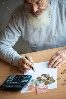 le concept – close up of old senior man hands with calculator and bills counting euro money at home.Older man writing notes on white sheet of paper.