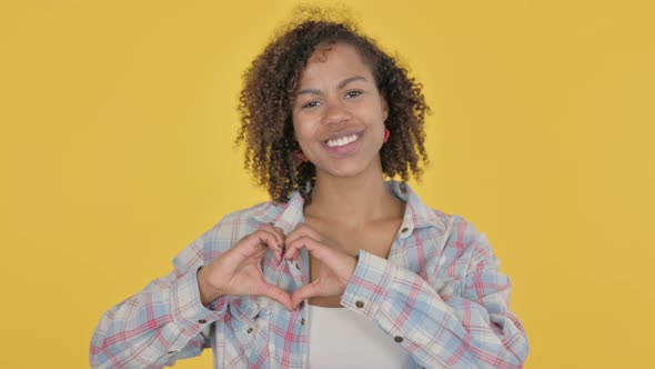 Young African Woman Showing Heart Shape By Hands on Yellow Background