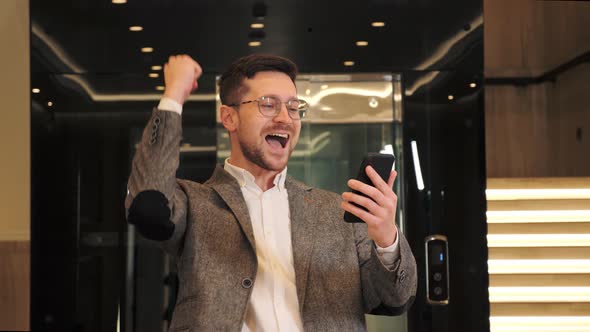 Happy Stylish Businessman Rejoices in Holiday Looking at the Mobile Phone